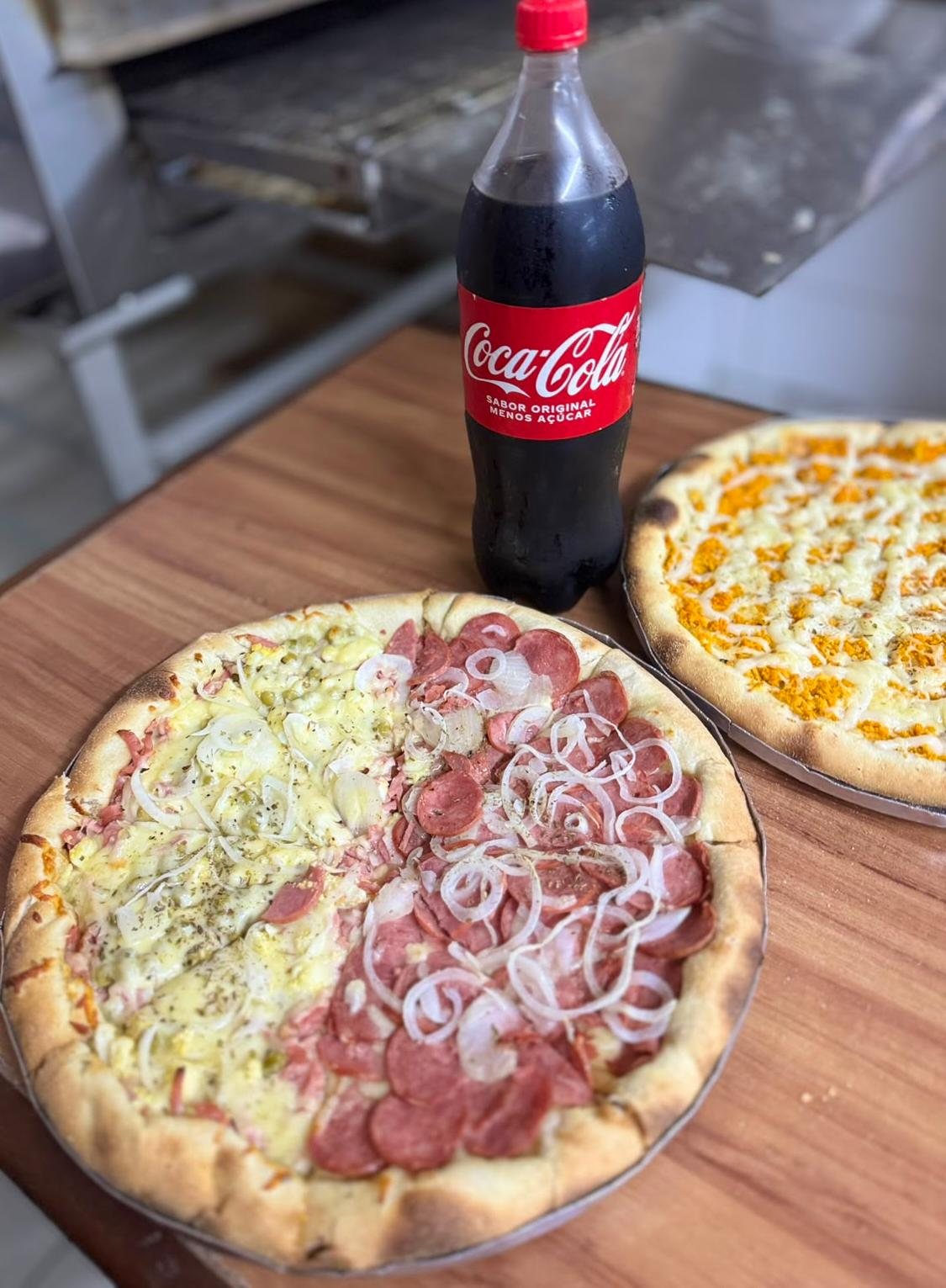 Pizza meio a meio com calabresa e presunto sobre a mesa, com uma pizza de queijo ao fundo