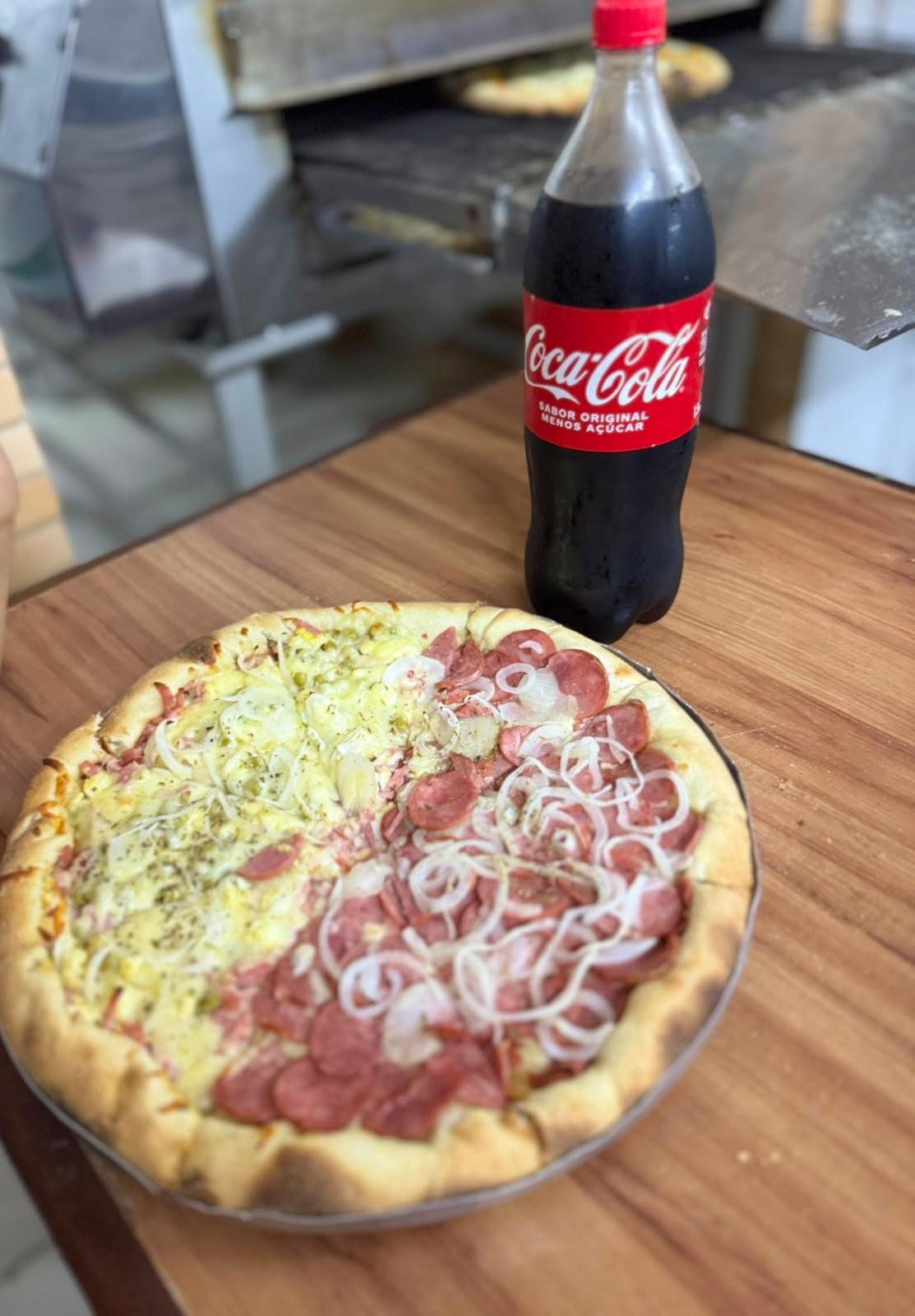 Pizza meio a meio recém-saída do forno da Bonna Pizza, com fumaça subindo, ao lado de uma garrafa de Coca-Cola